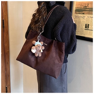 Detail of dark brown tote bag featuring checkered embossing and a cute bear charm