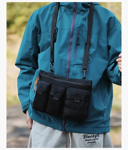 Detail of a black multi-pocket tactical crossbody bag with bright orange paracord zippers