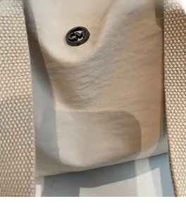 Détail du sac à bandoulière en nylon beige avec logo métallique rond et sangle tissée