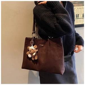 Detail of dark brown tote bag with quilted pattern, featuring a cute plush bear pendant