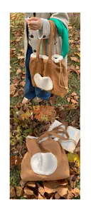 Brown suede tote bag with white plush trim and drawstring detail in autumn scene