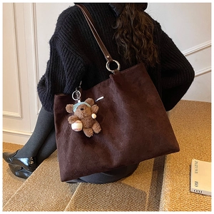 Detail of dark brown quilted tote bag with cute plush bear charm on a slim shoulder strap