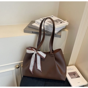 Detailed close-up of large brown leather tote bag featuring a decorative silk ribbon handle