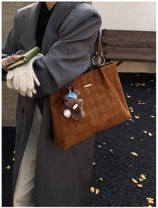 Brown suede tote bag with quilted pattern detail and bear pendant worn on shoulder