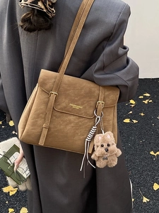 Sac fourre-tout en cuir marron mat avec boucle dorée et breloque chiot en peluche dans la rue