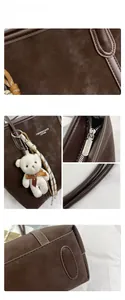 Detail of dark brown matte leather tote bag featuring a teddy bear charm and silver zipper