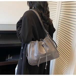 Vue latérale d'un sac seau gris matelassé avec cordon et poche avant zippée en métal