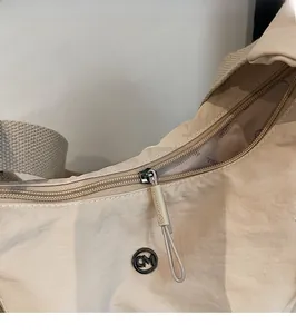 Détail du sac à bandoulière en nylon beige montrant le logo CM en métal et le curseur