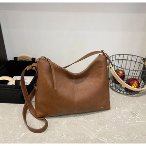Detail of a brown leather Hobo bag with gold zipper and adjustable strap on a marble surface