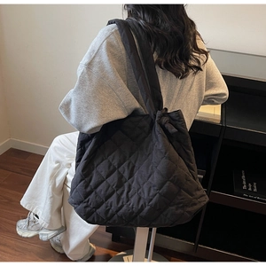 Détail d'un grand sac cabas noir matelassé avec bandoulière nouée porté à l'épaule