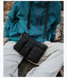 Detail of black tactical crossbody bag with multiple pockets and orange zipper pulls
