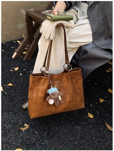 Detail of brown suede tote bag with quilted texture and a cute bear plush charm