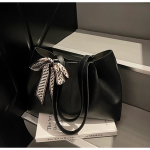 Close-up of black tote bag featuring a patterned silk scarf tied to the handle strap