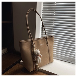 Detail of light brown matte tote bag with teddy bear charm in natural sunlight