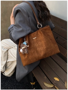 Detail of dark brown suede tote bag with quilted diamond pattern and bear charm