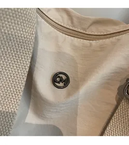 Détail du sac en nylon beige avec logo métallique CM et bandoulière texturée épaisse