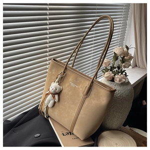 Detail of khaki suede tote bag with plush bear charm and fashion leather text