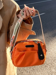 Orange pleated nylon crossbody bag with floral embroidered strap in outdoor setting