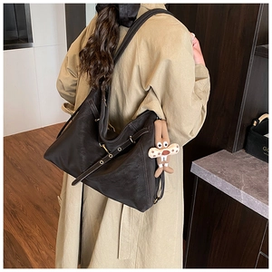 Detail of a large black vintage leather tote bag with a cute brown plush pendant