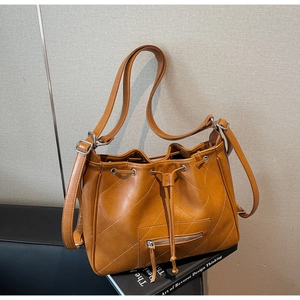 Détail d'un sac seau matelassé marron avec cordon et finitions argentées posé sur un livre