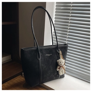 Detail of black matte leather tote bag with long shoulder straps and plush bear charm