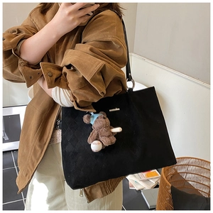 Detail of black quilted tote bag with metal logo and cute plush bear charm accessory