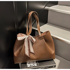 Detail of a brown PU leather tote bag with a patterned silk scarf on a book