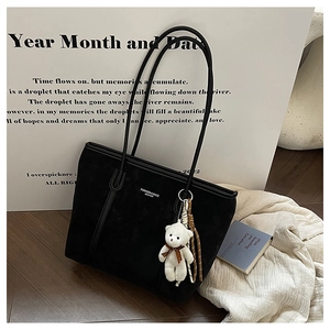 Detail of minimalist black tote bag with plush bear charm and woven leather trim