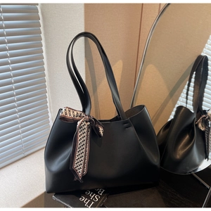 Detail of black matte leather tote bag with a silk scarf tied on the handle
