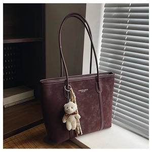 Detailed macro of burgundy suede tote bag with teddy bear charm and fashion text