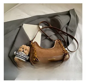 Detail of brown crescent bag with gold chain, suede stitching and teddy bear charm