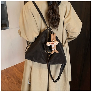 Detail of a black soft leather tote bag featuring a cute beige rabbit plush charm