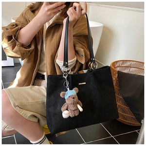Detail of black tote bag featuring diamond pattern texture and cute teddy bear charm