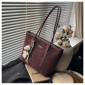 Detail view of burgundy frosted leather tote bag with plush bear charm and text embossing