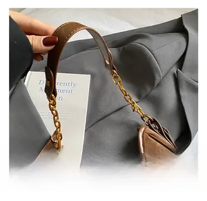 Detail showing brown suede texture with leather stitching and gold metal chain strap