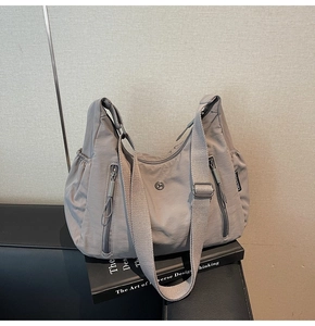 Détail d'un grand sac à bandoulière en nylon gris avec poches zippées et logo métal