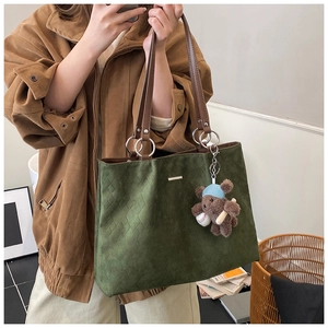 Detail of dark green suede tote with diamond quilting and bear charm on shoulder strap