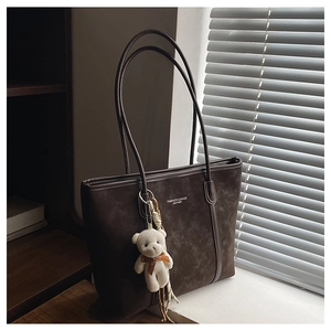 Detail of dark brown suede tote bag with white text and cute teddy bear charm