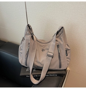 Détail du sac bandoulière en nylon gris montrant la texture durable et le logo métallique