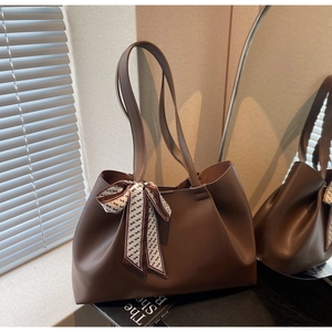Close-up of brown faux leather tote bag featuring decorative H-pattern silk scarf handle