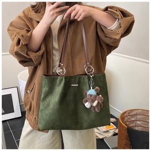 Detail of dark green suede tote bag featuring a cute brown teddy bear charm with a cap
