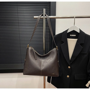 Detail of dark brown leather tote featuring a wide shoulder strap and gold zipper