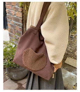 Detailed view of brown sherpa tote bag with heart patch worn by model in street setting