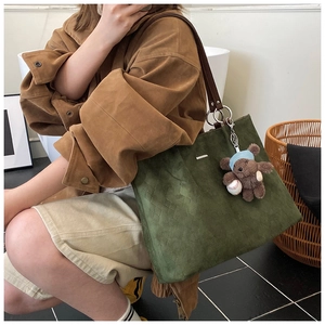 Close-up of olive green suede tote bag featuring a cute teddy bear plush charm and brown strap