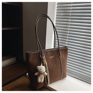 Detail of dark brown leather tote bag with a cute bear charm and woven rope accent