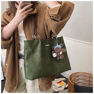 Close-up of green suede tote bag with brown leather straps and a cute teddy bear charm