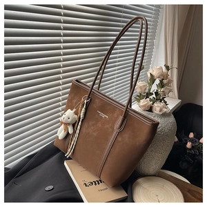 Close-up of coffee brown suede tote bag featuring a plush bear charm and woven rope detail