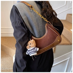 Detail of dark brown crescent bag with suede texture, gold chain and bear charm