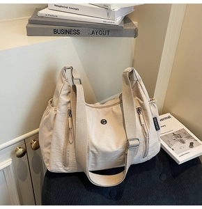 Détail du sac bandoulière en nylon crème avec poches zippées et large sangle tissée