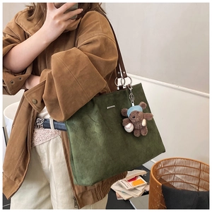 Detail of green suede tote bag with woven texture, metal logo and cute bear charm